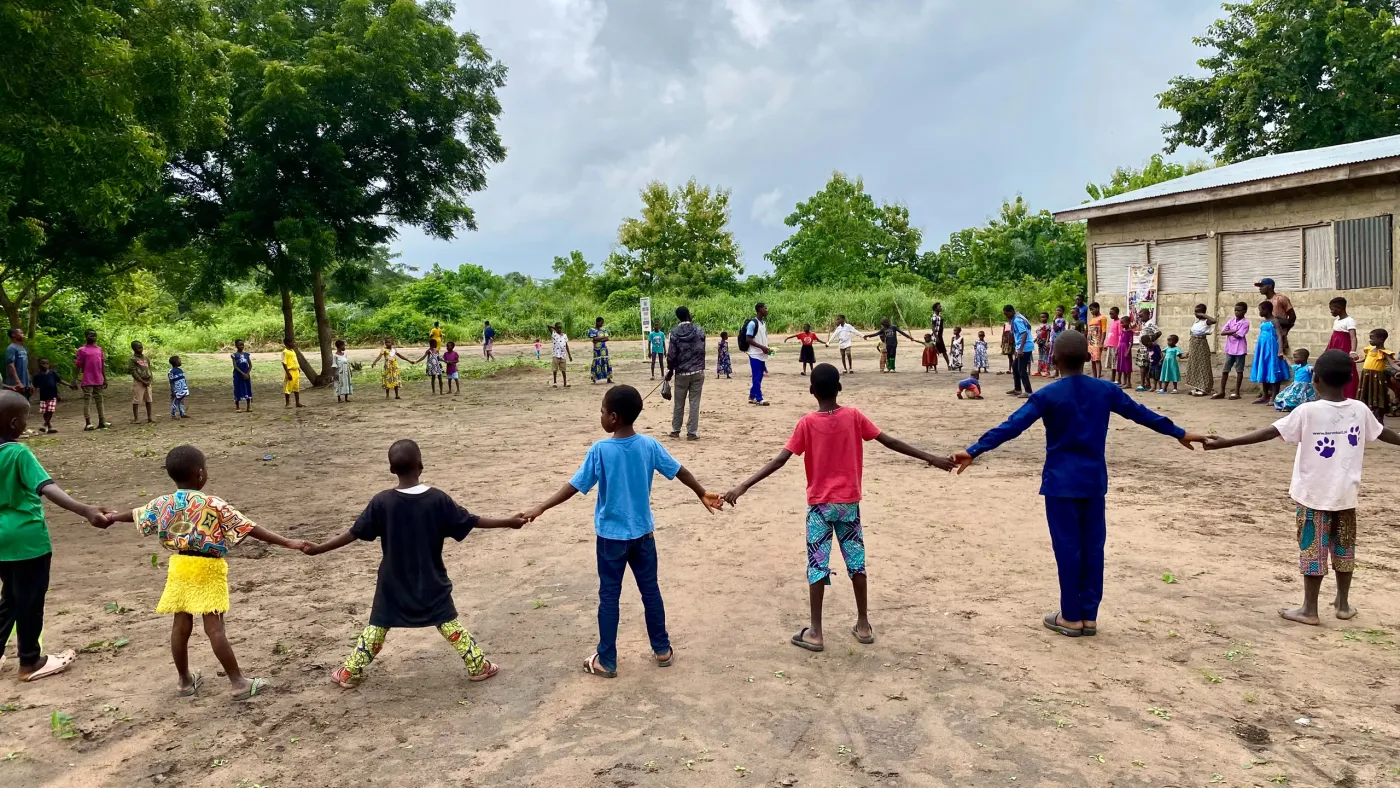 Children holding hands in a large circle on a village field in Togo